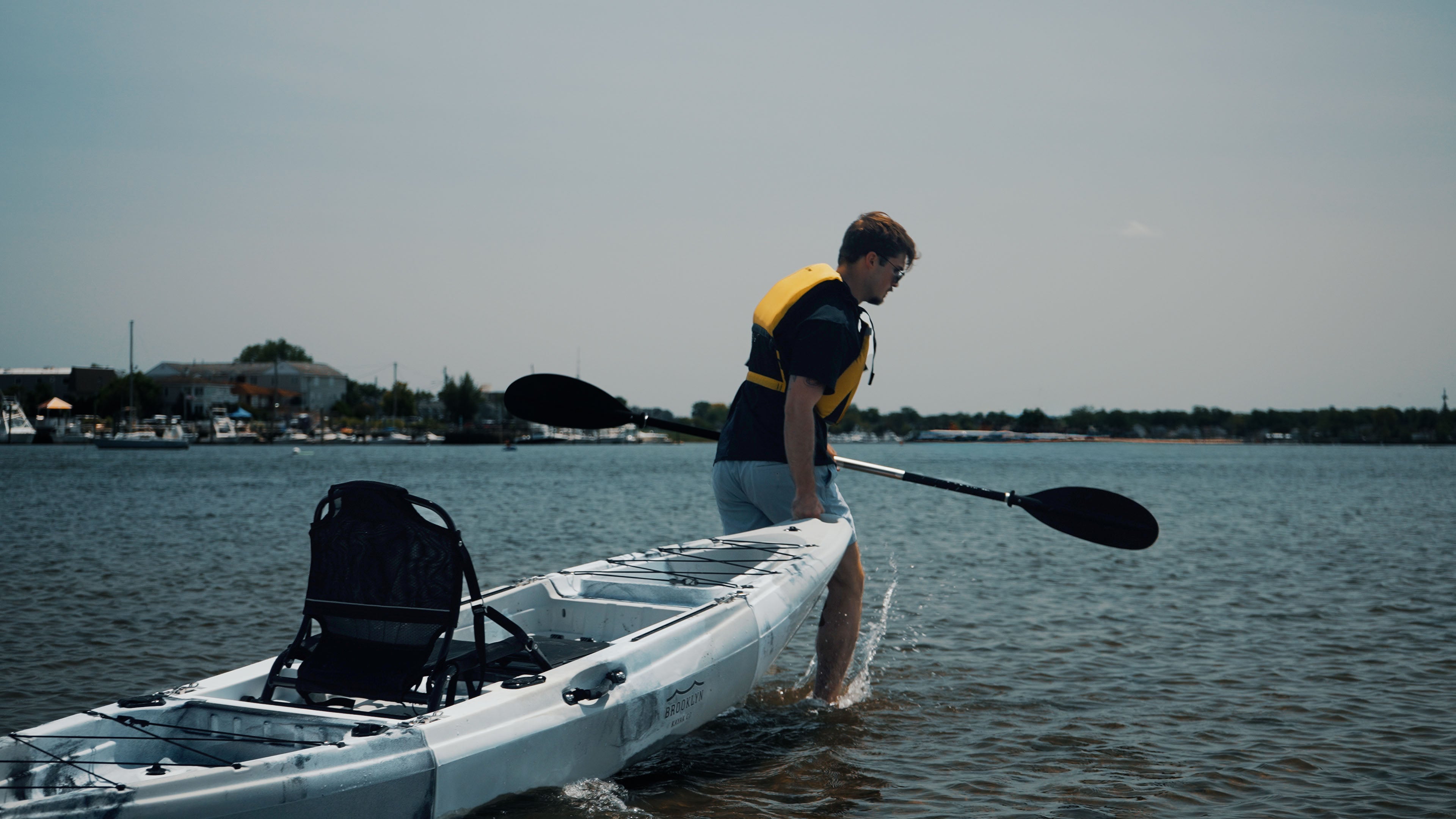 man carrying a single kayak out into the water - Brooklyn Kayak Company